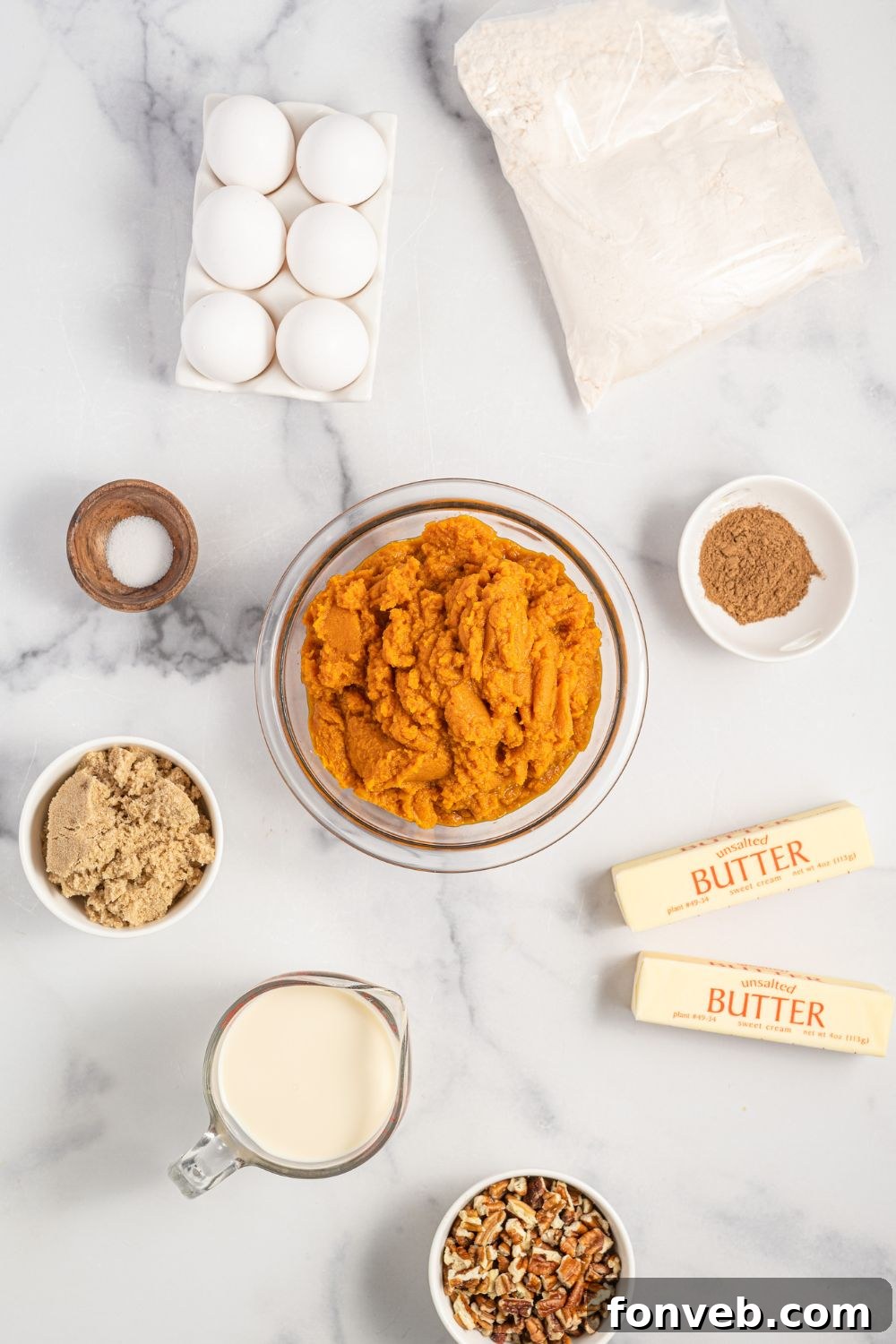 An assortment of fresh ingredients for Pumpkin Dump Cake laid out on a marble countertop, including canned pumpkin puree, a box of yellow cake mix, pecans, brown sugar, and a small bowl of pumpkin pie spice.
