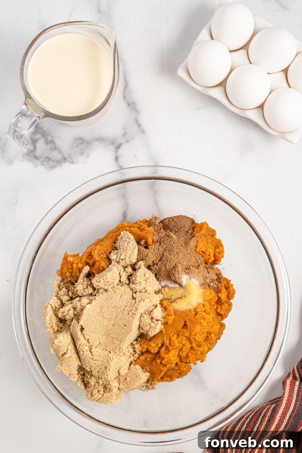 A glass bowl filled with rich orange pumpkin puree, light brown sugar, and a blend of pumpkin pie spices, ready to be mixed for the cake base.