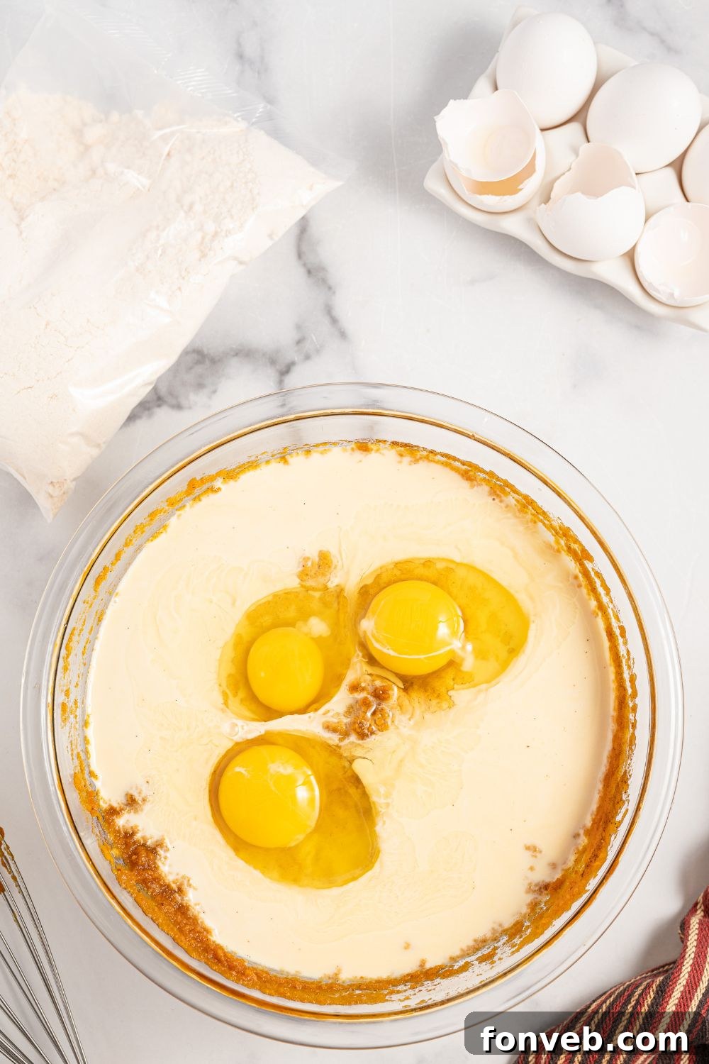 A creamy pumpkin mixture in a glass bowl, with eggs and evaporated milk added, being whisked until smooth and well combined.