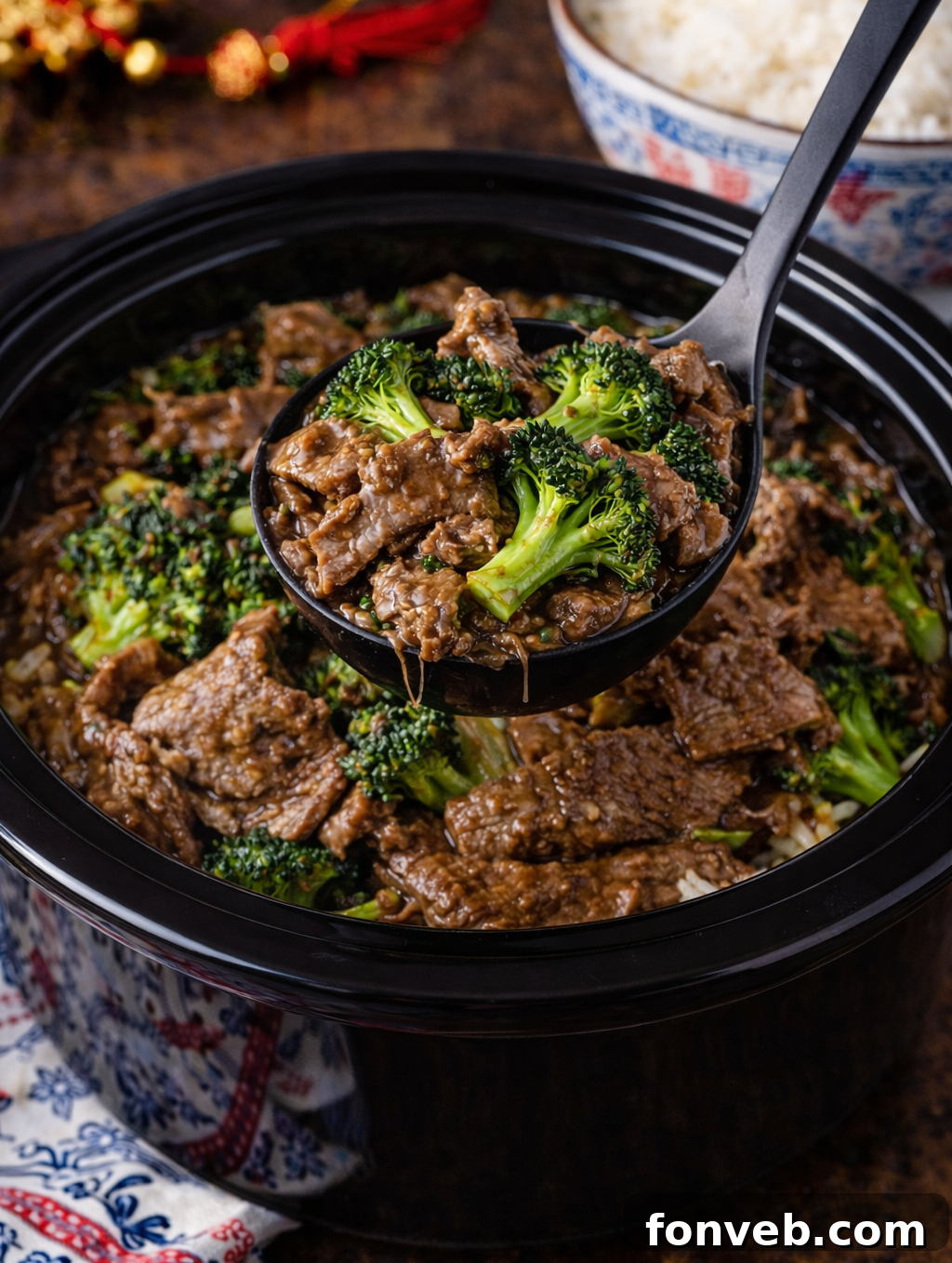 Slow Cooker Beef & Broccoli in a black slow cooker with a spoon lifting some up