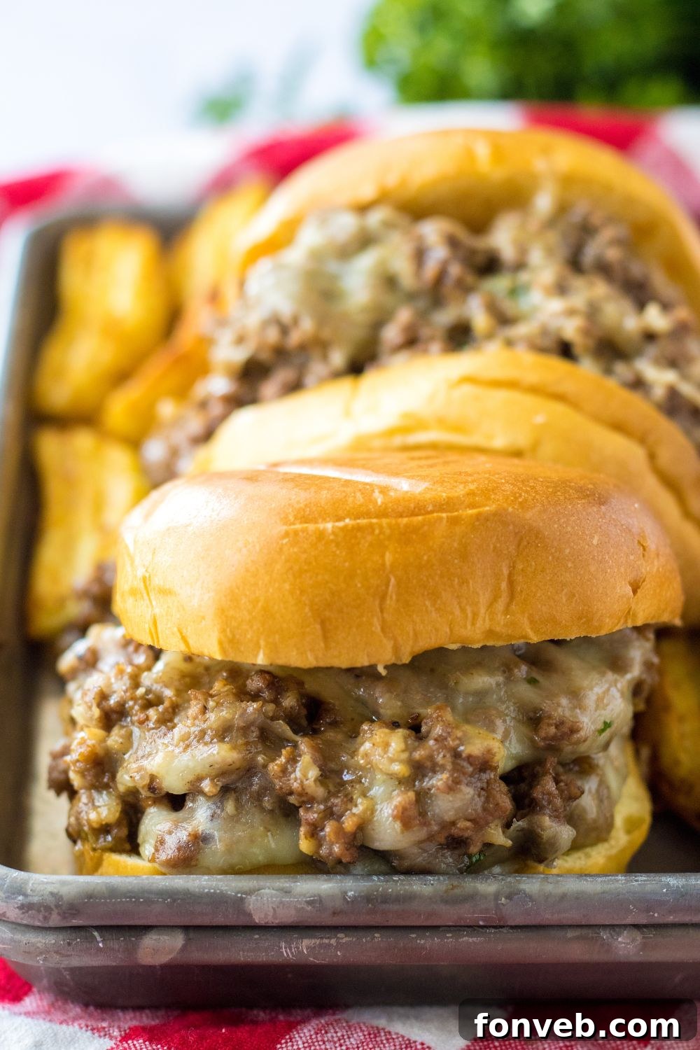 french dip sandwiches on a metal tray with potato wedges behind it 