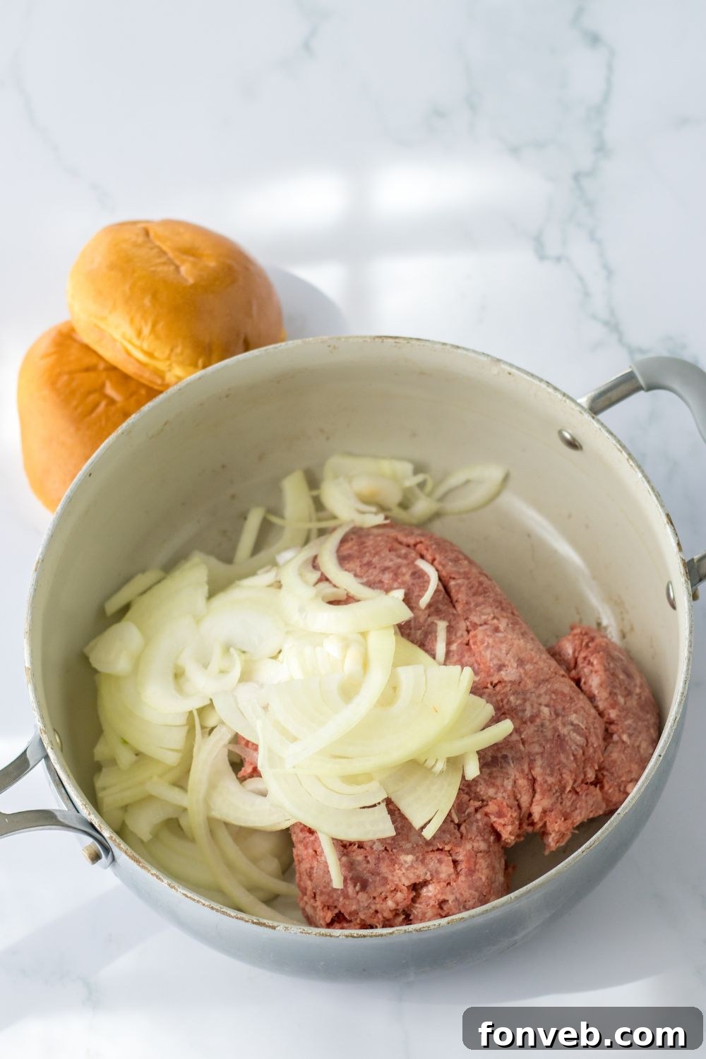 raw ground beef and sliced onions in a pan on stovetop