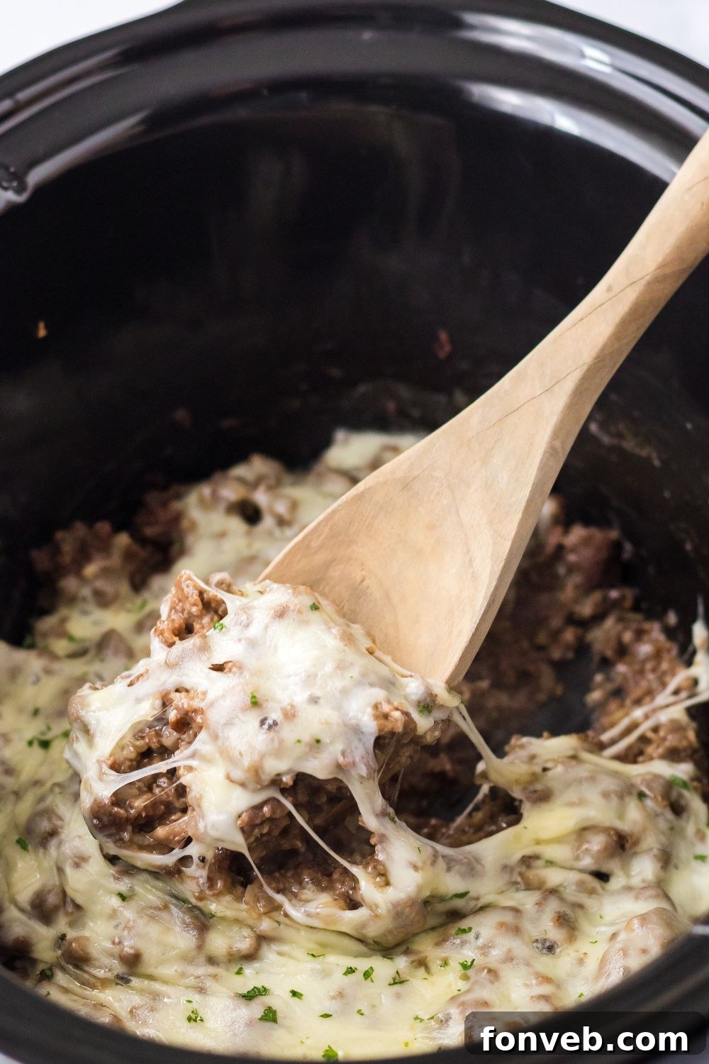 french dip mixture in slow cooker being lifted out with wooden spoon 