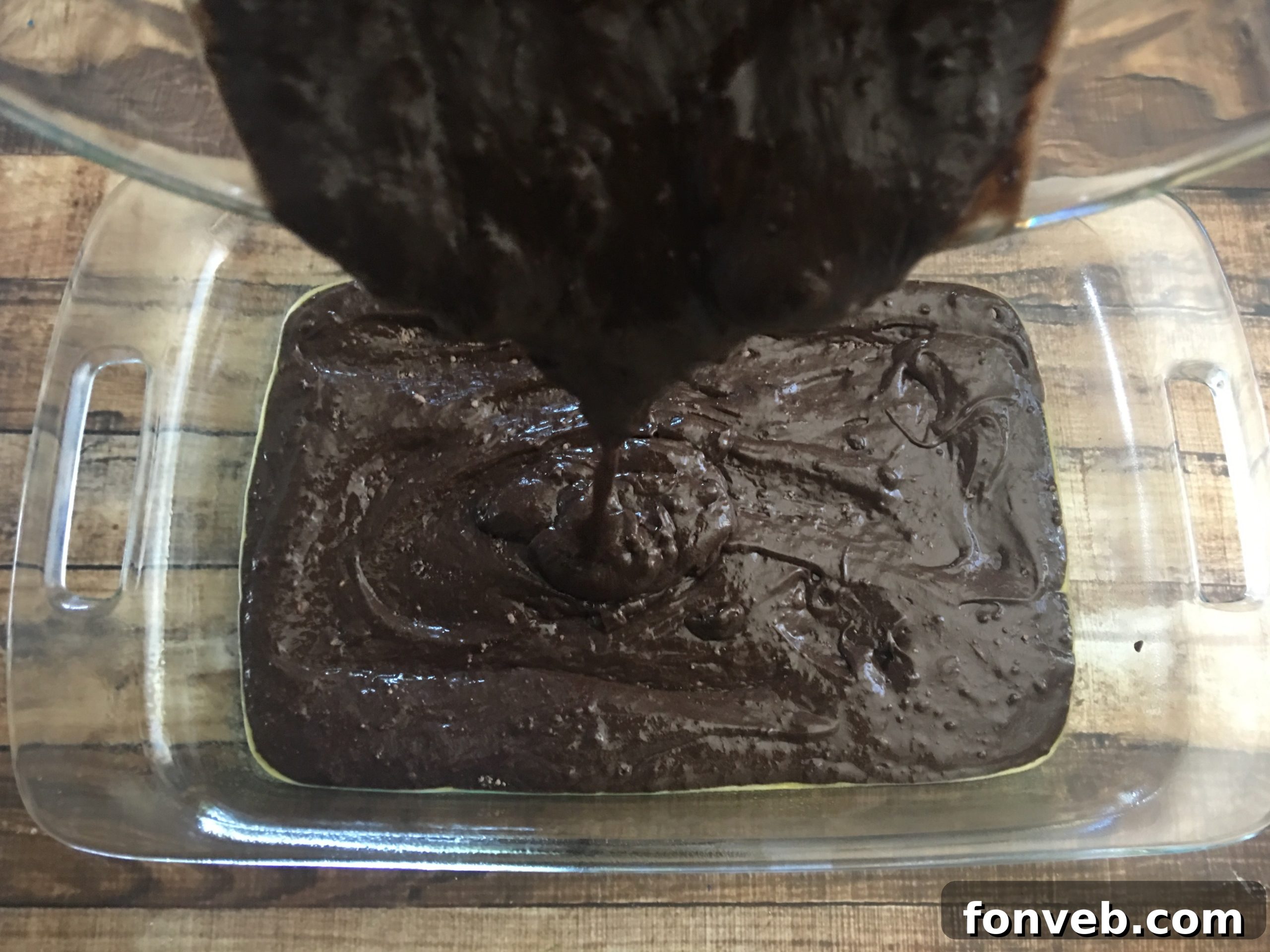 Peanut butter and cream cheese mixture being spread in dollops over the chocolate cake batter in a baking dish