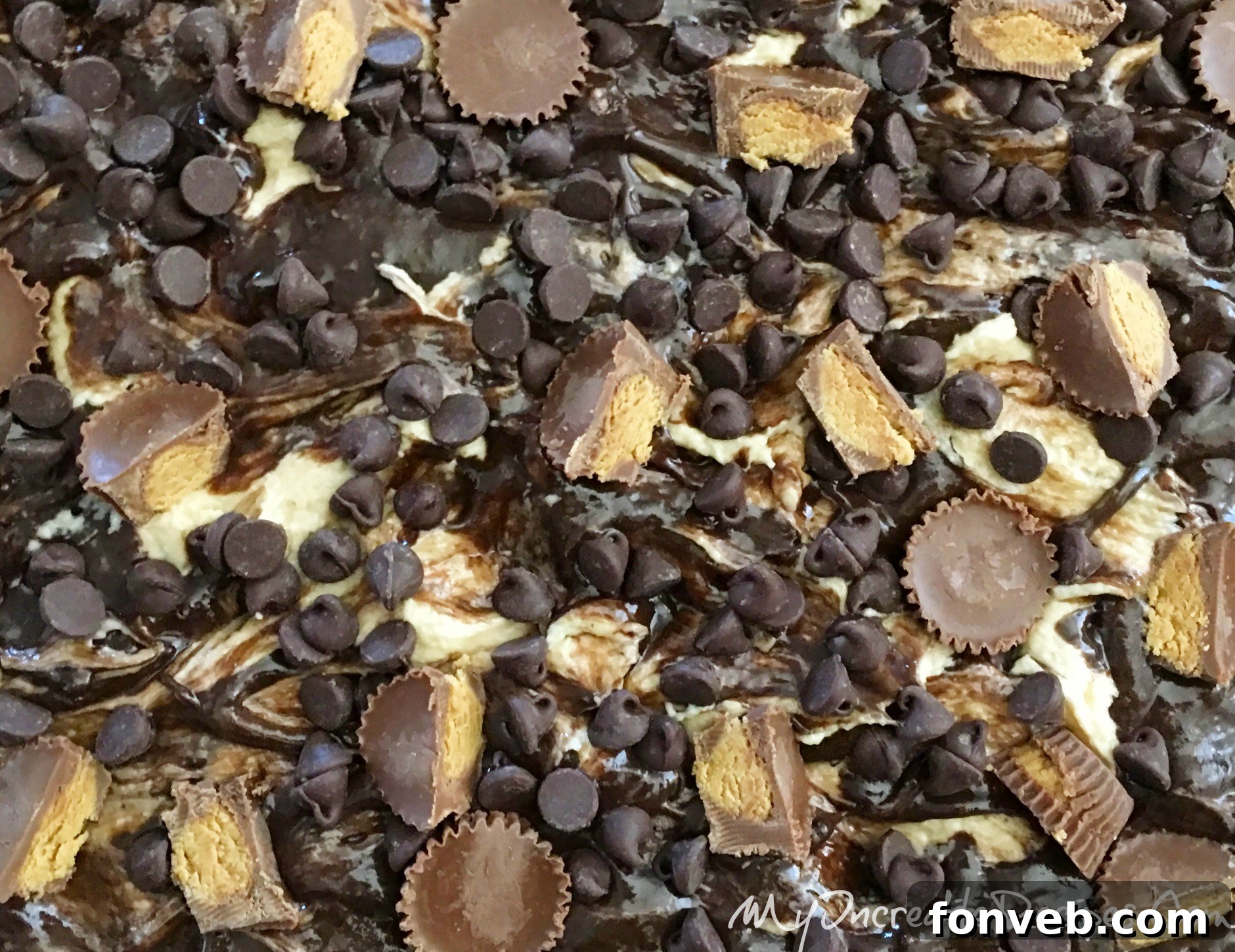 Raw cake batter with swirls of peanut butter and cream cheese, topped with Reese's cups and chocolate chips, ready for baking
