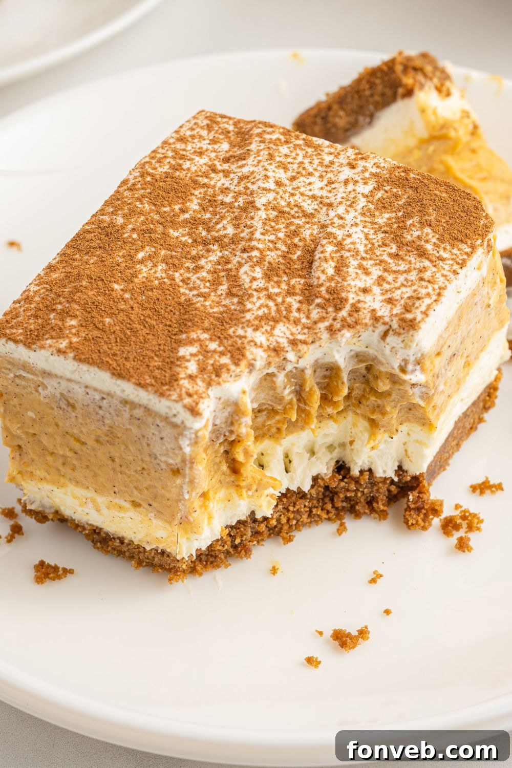 A plate with a slice of pumpkin lush dessert, with a bite taken out, indicating its creamy texture.