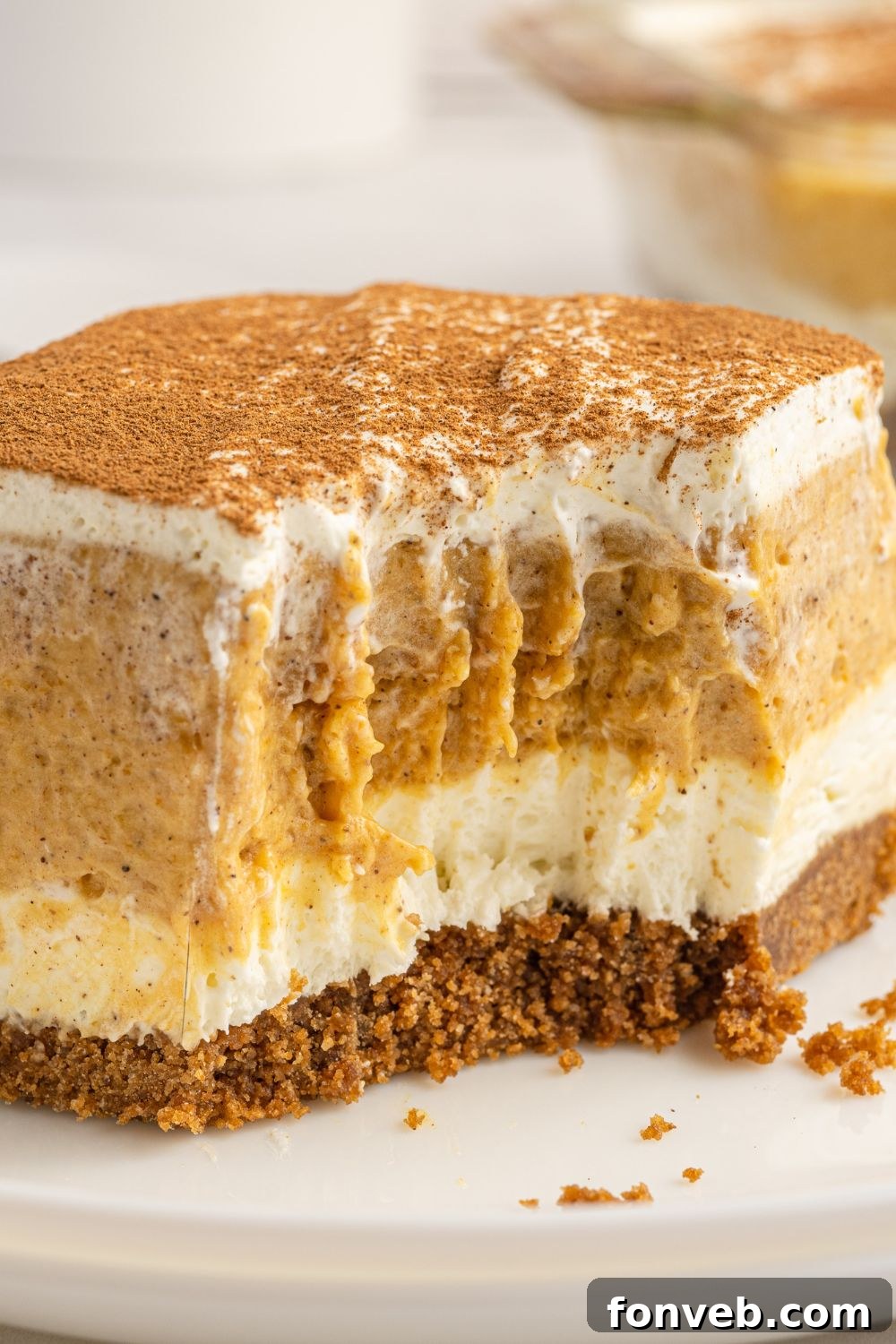 A close-up of a pumpkin lush dessert slice on a plate, with a bite taken out, emphasizing its appealing layers.