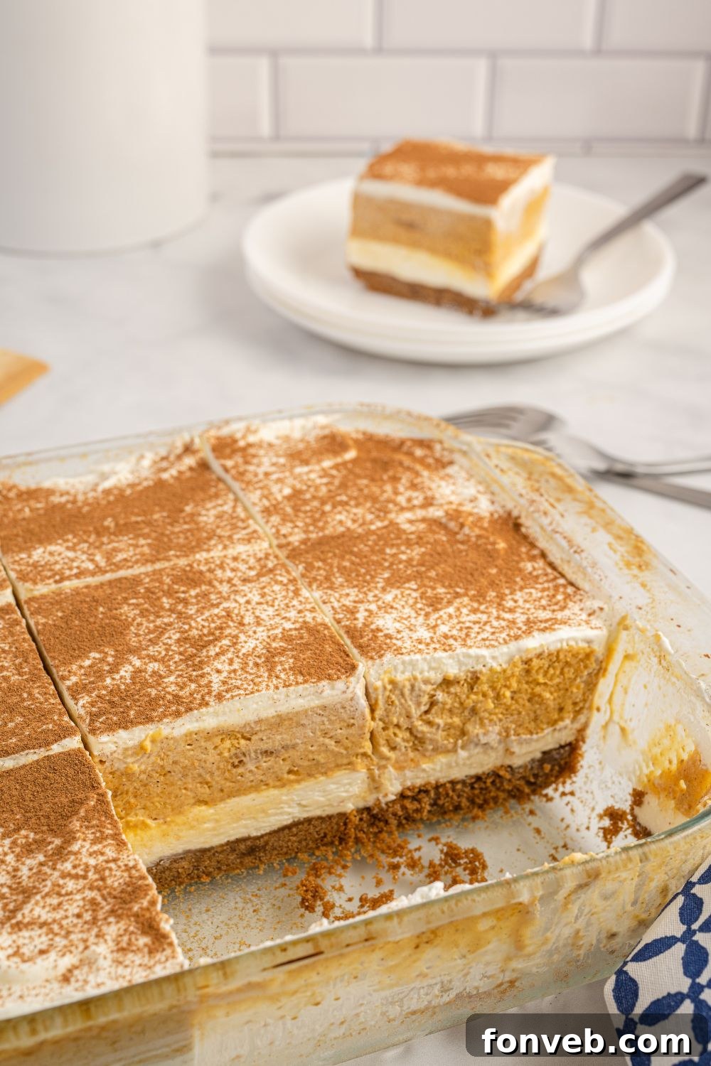 A pan of pumpkin lush dessert with a single serving plate in the background, creating a warm, inviting scene.