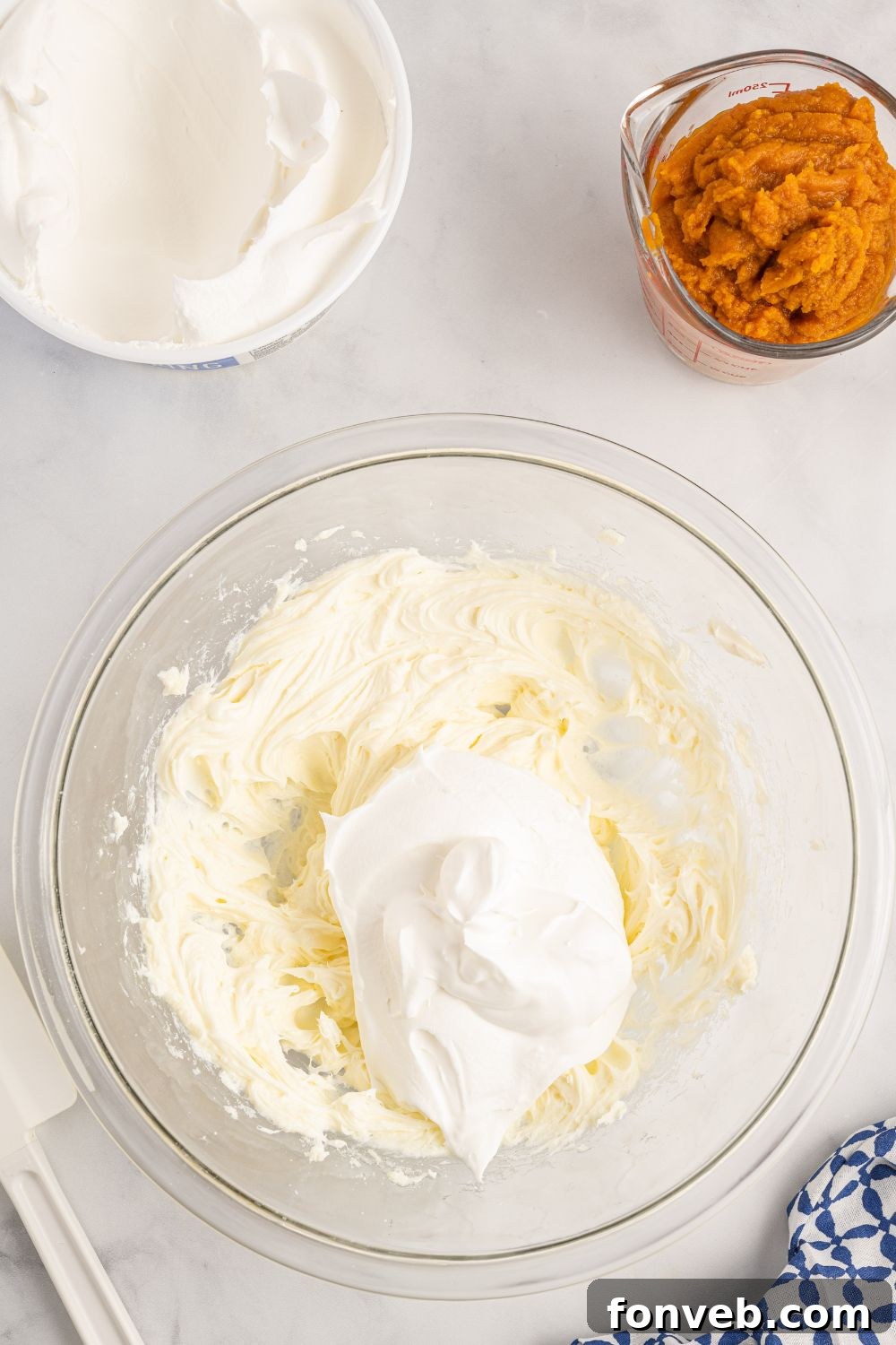 A creamy whipped topping mixture in a glass bowl, prepared for one of the dessert layers.