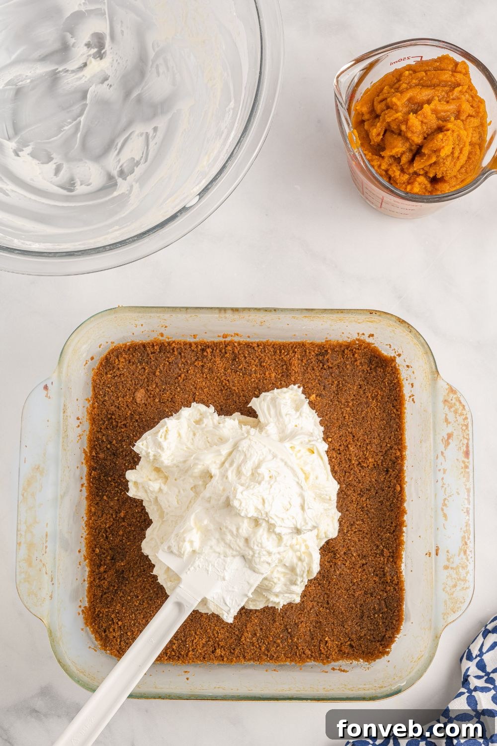 The cream cheese mixture being smoothly spread over the gingersnap crust in an 8x8 baking pan.