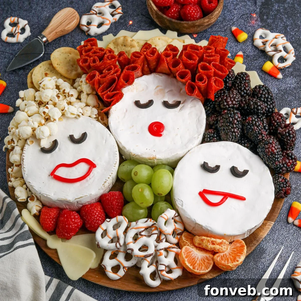 Overhead view of a Hocus Pocus Charcuterie Board featuring three Brie cheese wheels decorated as the Sanderson Sisters, surrounded by popcorn, pepperoni, various fruits, and crackers on a wooden board.