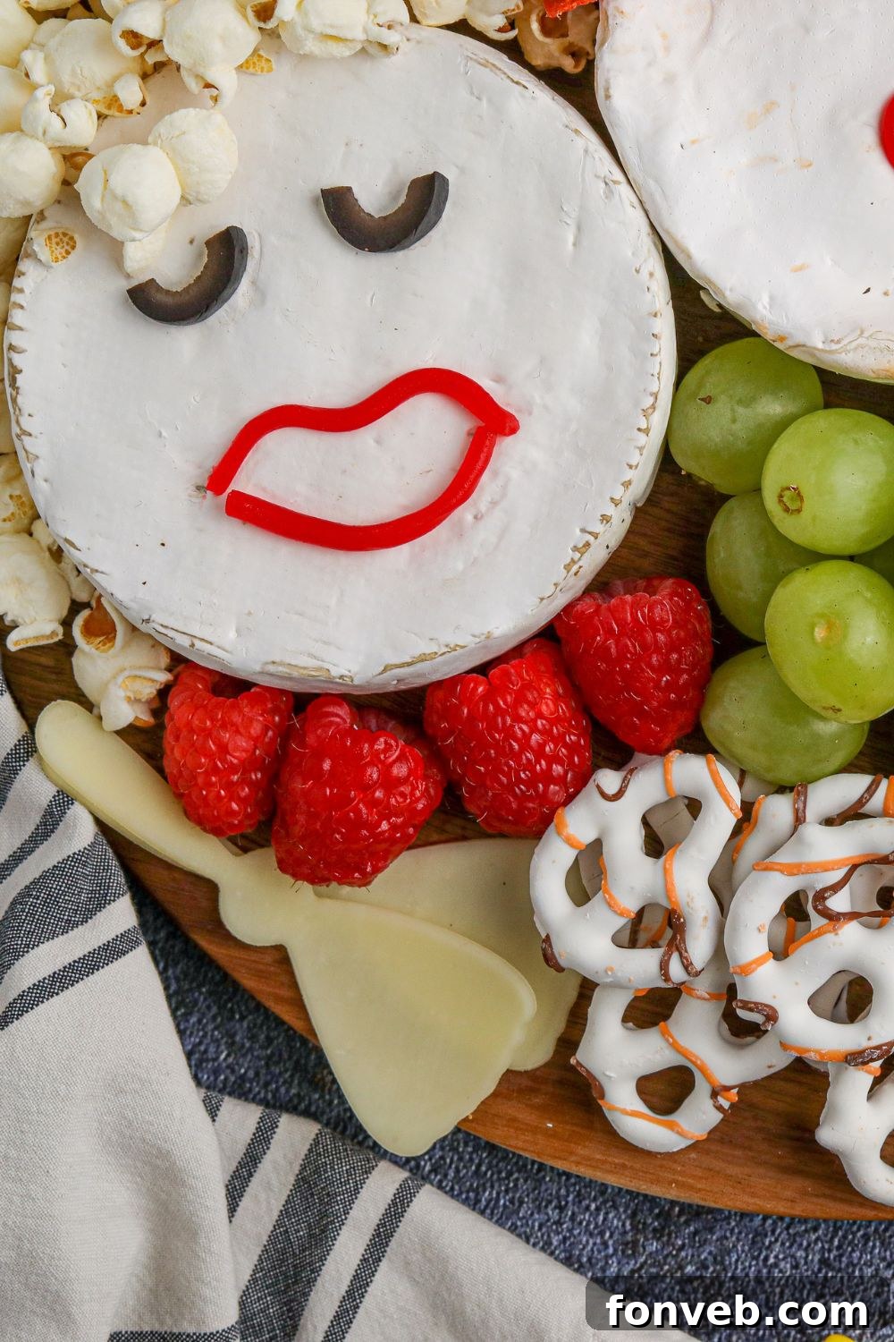A close-up, artistic shot of a Brie cheese wheel charcuterie board, highlighting the intricate details of the Sanderson Sisters' faces and surrounding snacks.