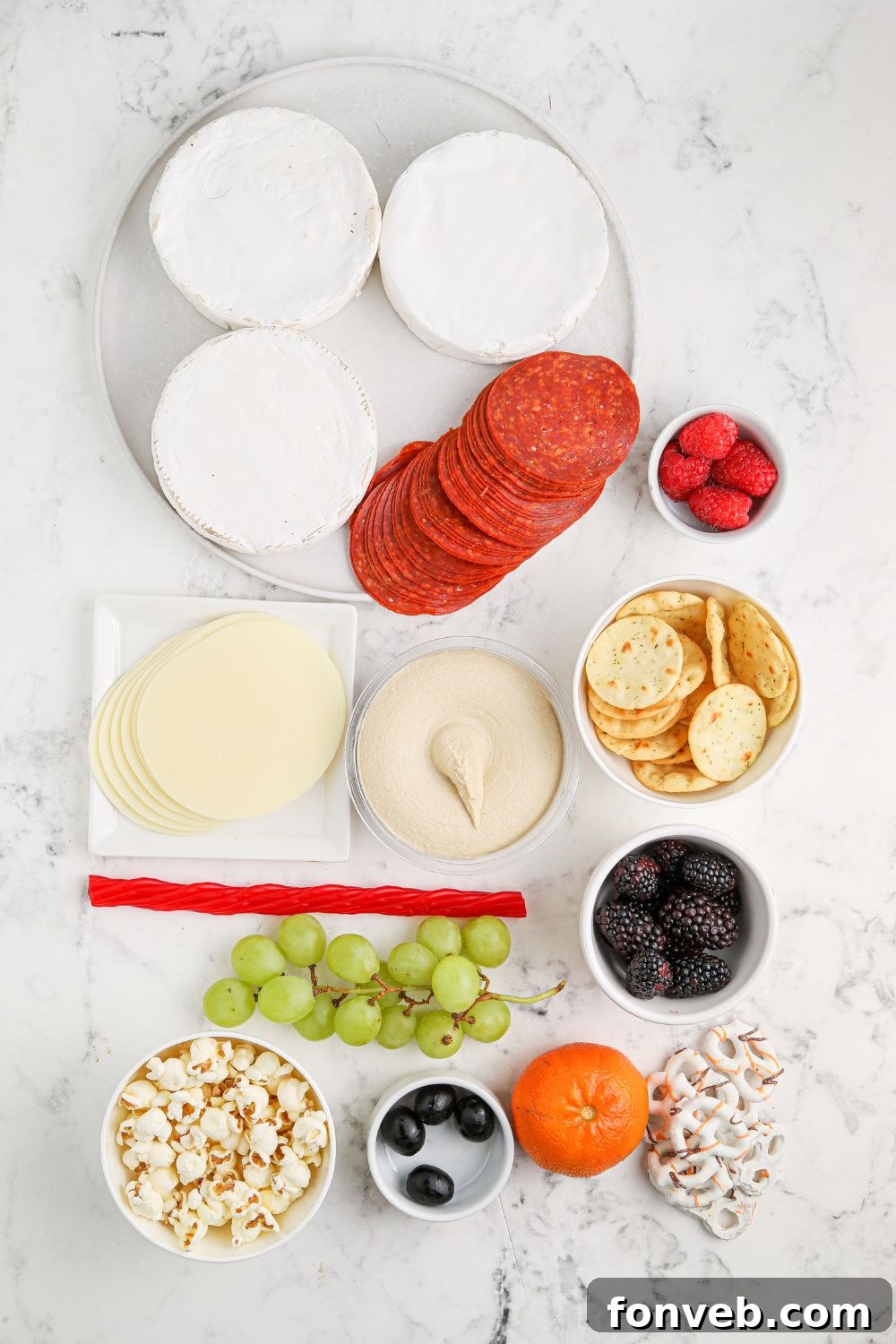 Assorted ingredients like Brie cheese, popcorn, pepperoni, various fruits, and olives laid out on a table, ready to be assembled into the Hocus Pocus charcuterie board.