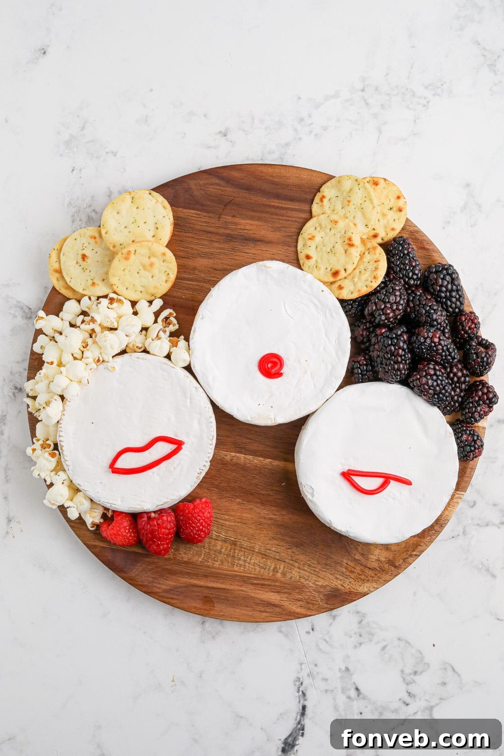 A close-up view of the Hocus Pocus charcuterie board being assembled, showing Brie cheese wheels, pepperoni, and other ingredients carefully arranged on a wooden board.