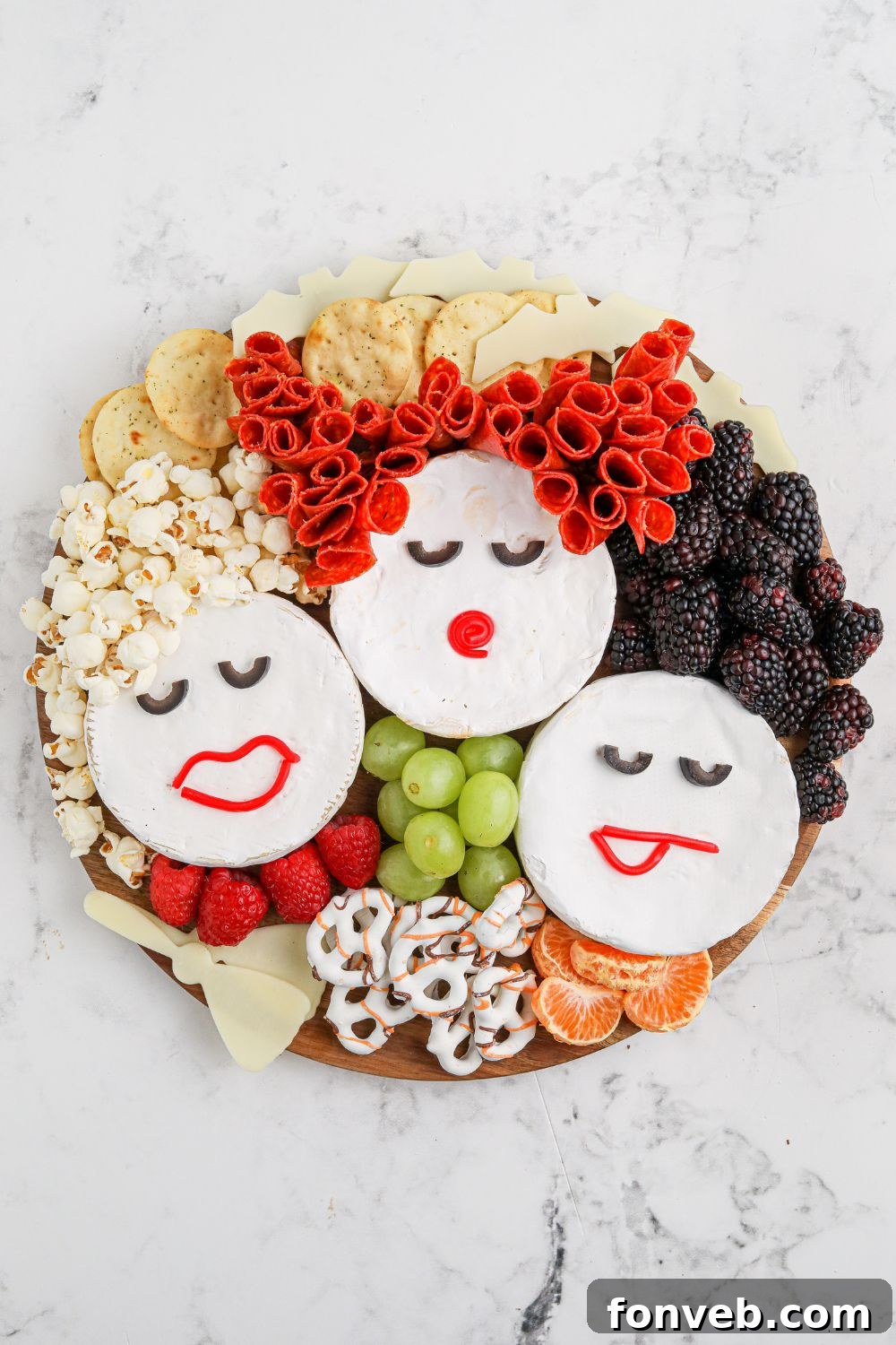 The Hocus Pocus charcuterie board mid-assembly, showcasing the three Brie cheese wheels adorned as the Sanderson Sisters' faces, with popcorn, pepperoni, and blackberries forming their hair.