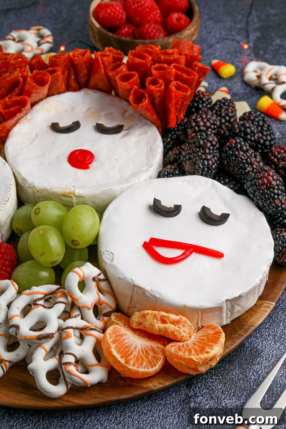 A rustic wooden tray for a Hocus Pocus theme, adorned with colorful oranges, green grapes, and various other snacks, illustrating a vibrant charcuterie board setup.