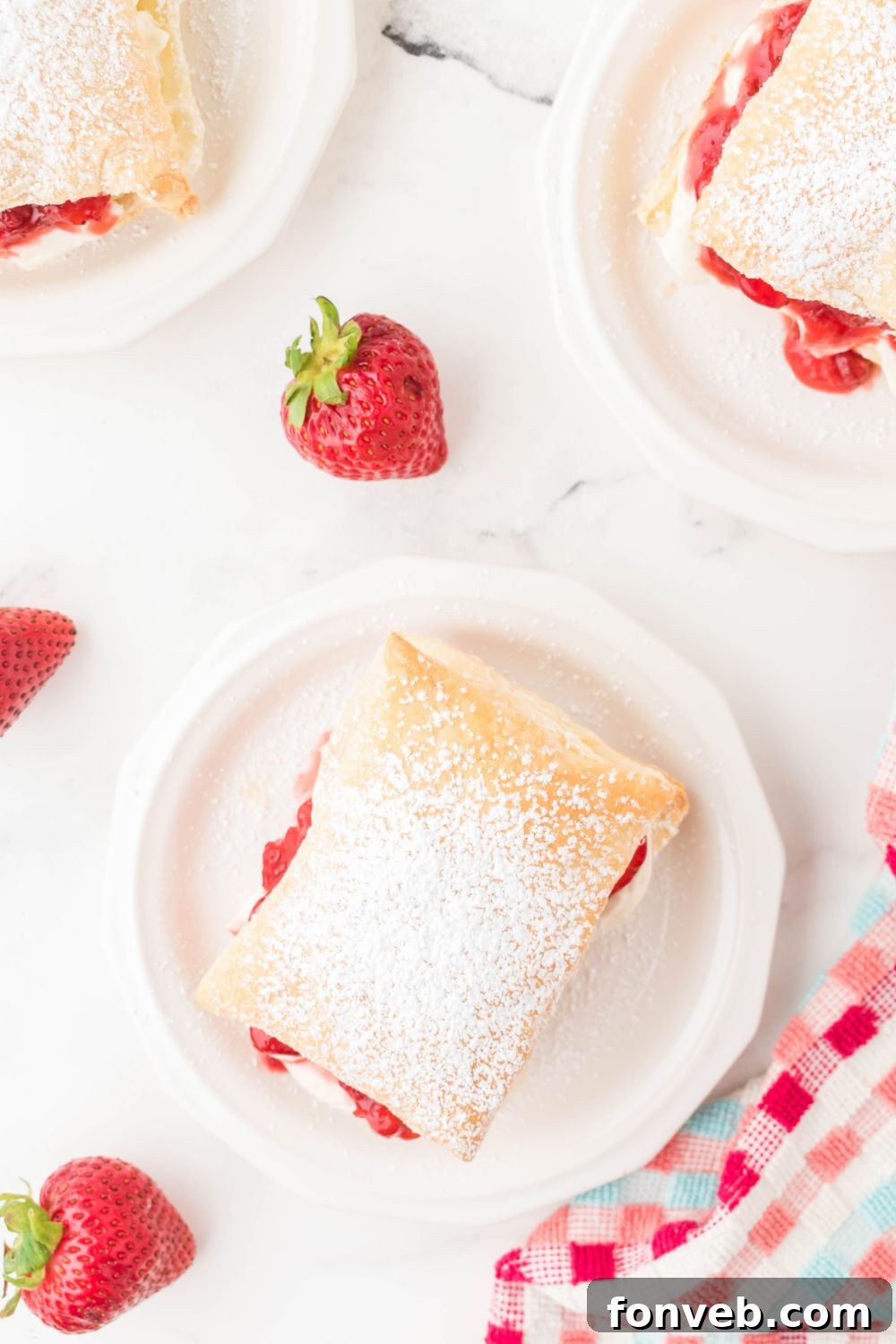 strawberries puff pastries on plates with berries around it on table