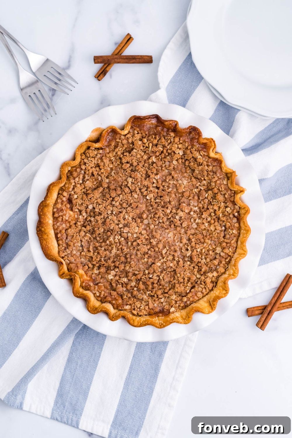 Spiced Apple Crumble Cheesecake Pie 7 Apple Crumble Cheesecake Pie on table with cinnamon sticks and towel by pan