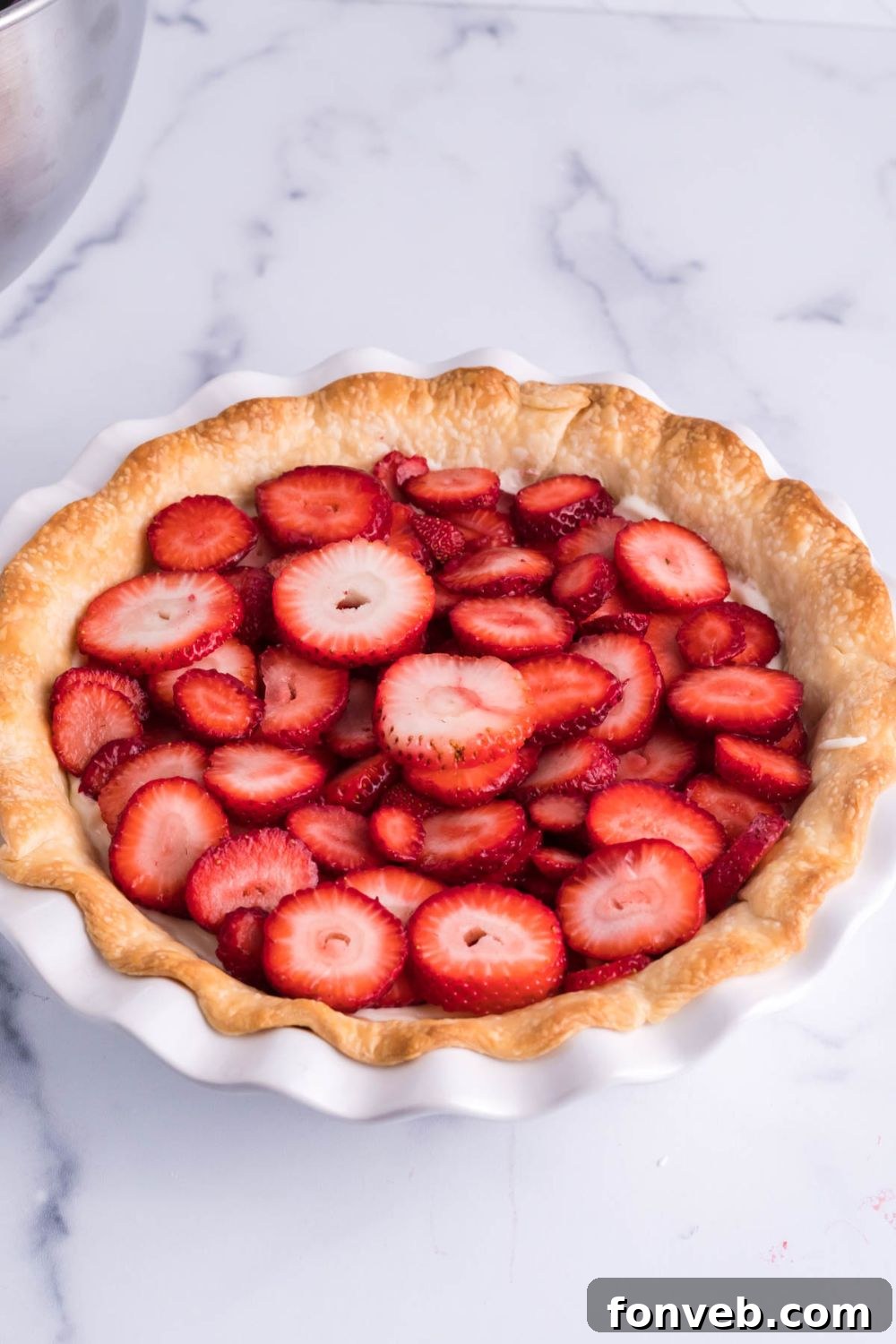 Thinly sliced fresh strawberries arranged neatly over the cream cheese filling in the pie crust, ready for the jello topping.