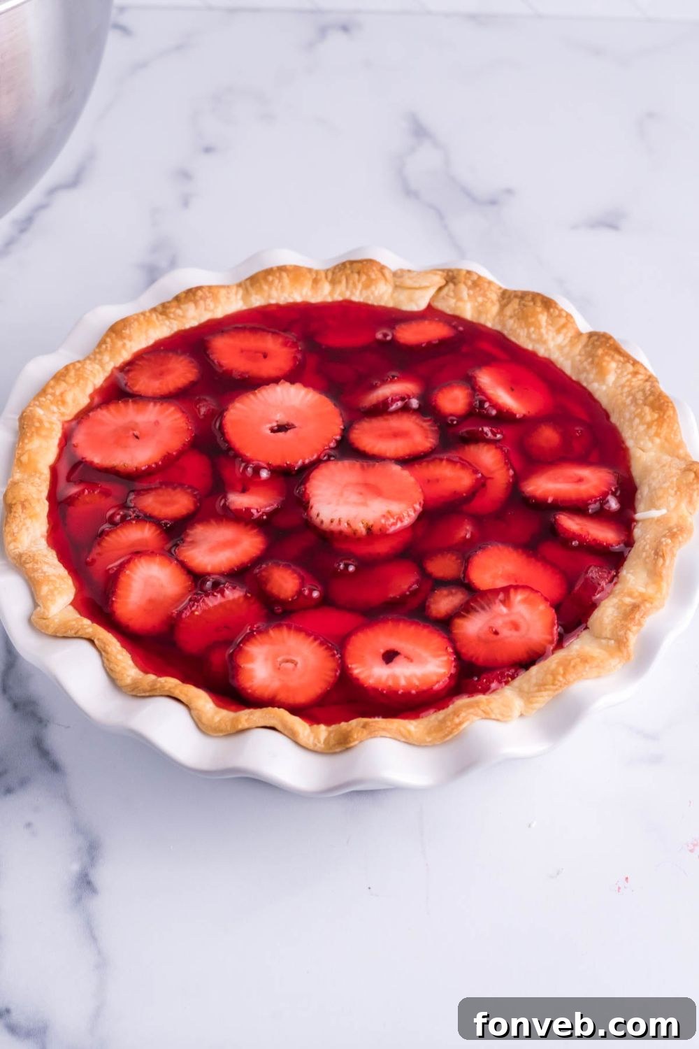 A shimmering red jello mixture being carefully poured over the fresh strawberries in the pie, filling the crust and creating the top layer.