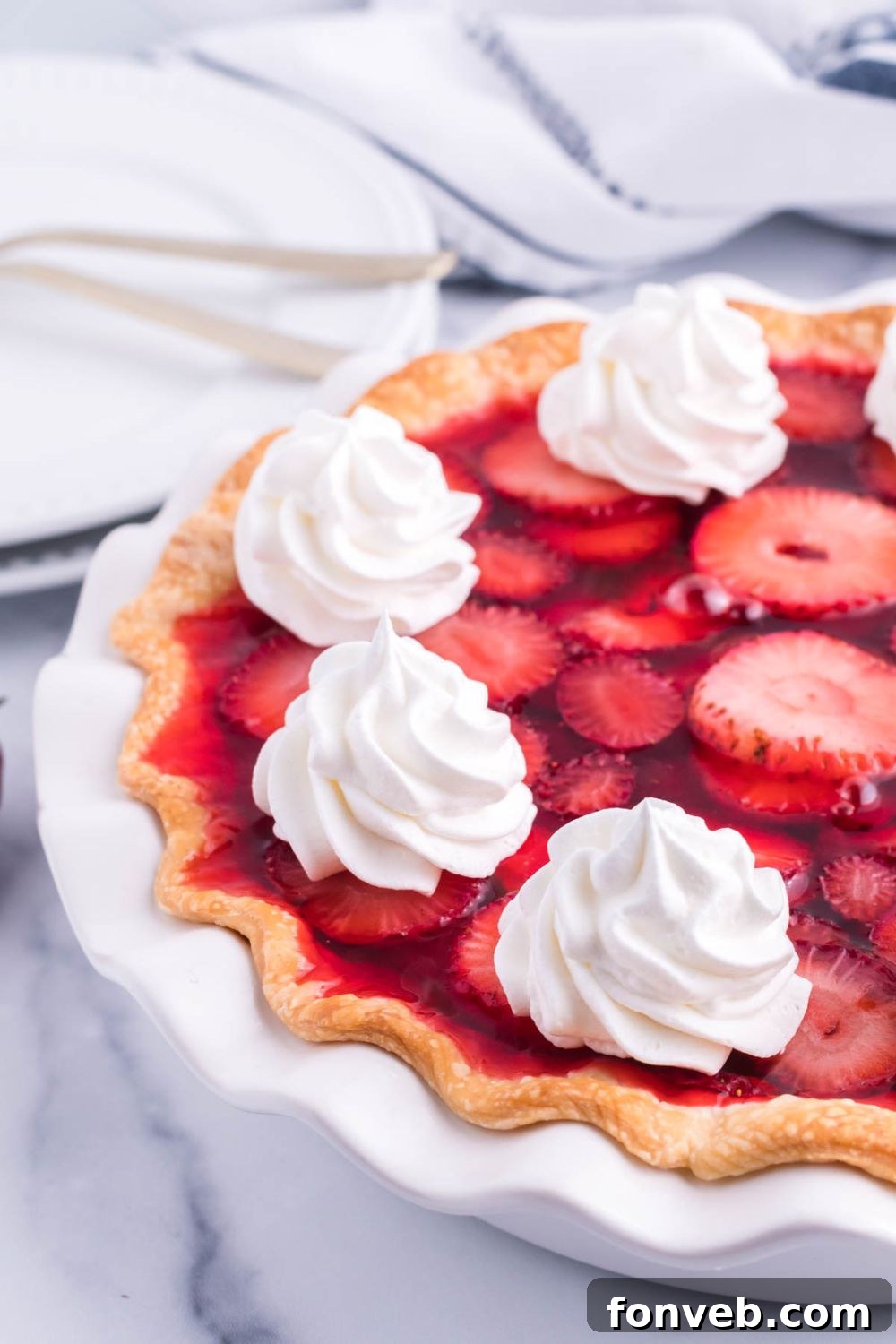 A tantalizing side view of half of a Strawberry Cream Cheese Pie still in its pan, revealing the beautiful layering of crust, white filling, and red strawberry topping.