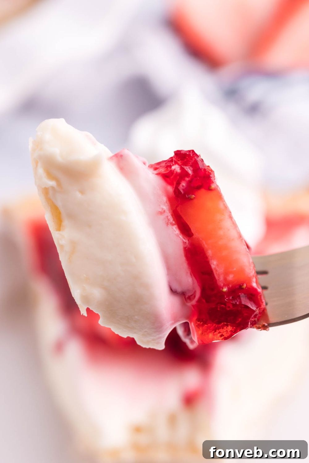 A detailed close-up view of a slice of Strawberry Cream Cheese Pie held on a fork, showing the creamy filling and a piece of fresh strawberry.