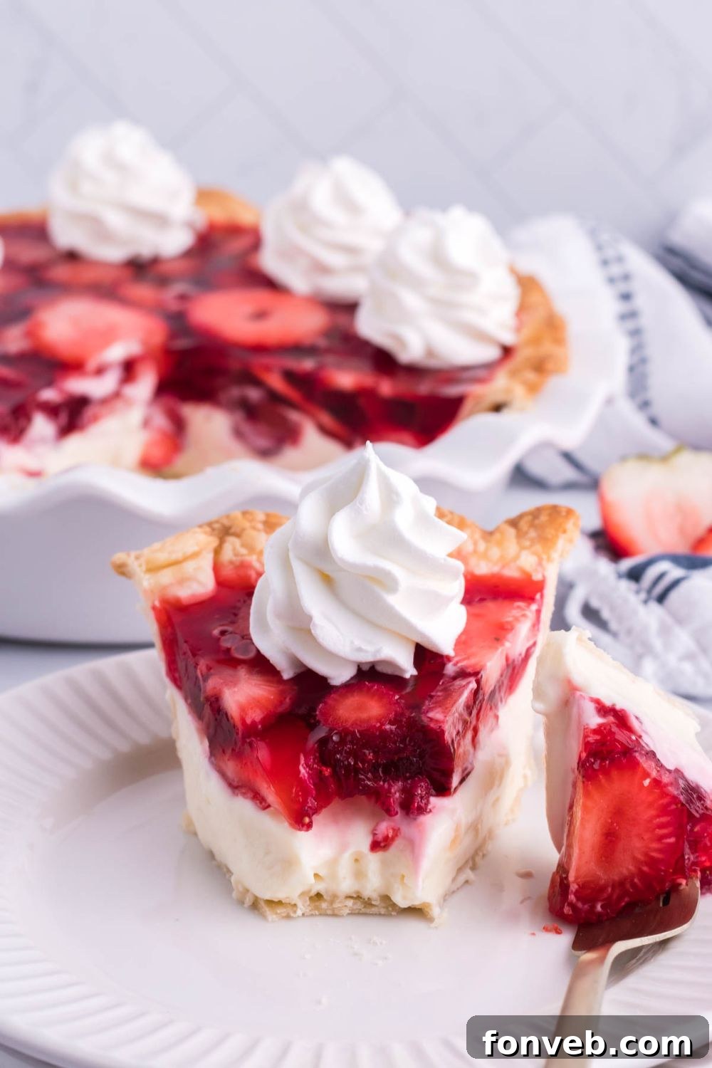 A close-up view of a slice of Strawberry Cream Cheese Pie on a white plate, with a small bite already taken, revealing the smooth cream cheese layer and the refreshing strawberry topping.