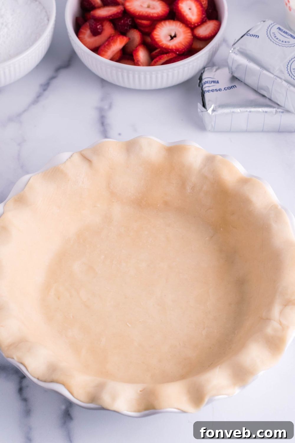 A rolled out pie crust neatly pressed into a metal pie pan, ready for pre-baking, showing crimped edges.