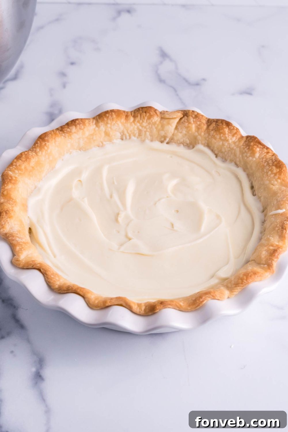 A side view of the cream cheese filling smoothly spread inside a pre-baked pie crust, highlighting the initial layer of the pie.