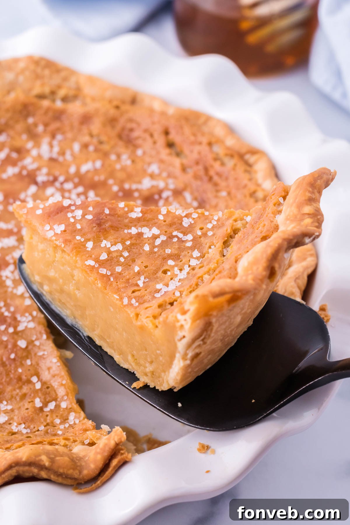 Golden Sweetheart 3 A freshly baked Honey Pie, with its golden crust and shimmering filling, being carefully lifted from a pristine white pie dish.