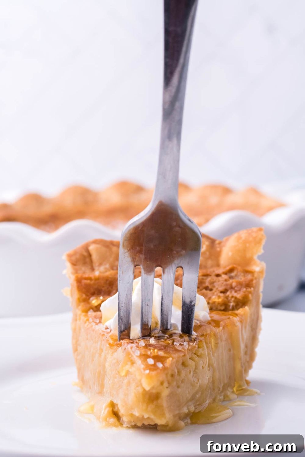 Golden Sweetheart 6 A fork delicately rests in a slice of golden honey pie, artfully placed on a plate on a rustic wooden table.