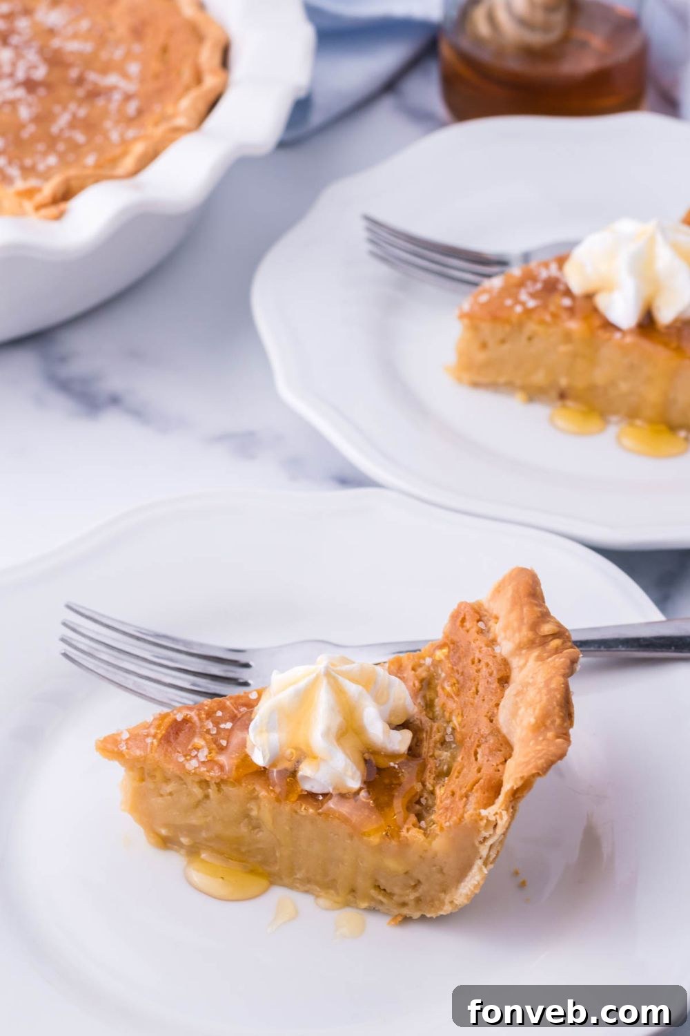 Golden Sweetheart 7 A perfectly baked slice of honey pie on a clean white plate with a fork, with a full honey pie in a pie dish elegantly blurred in the background.