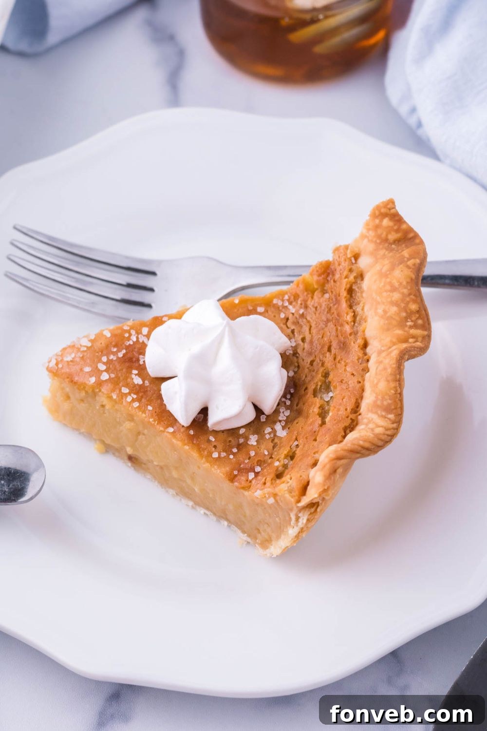 Golden Sweetheart 9 A slice of honey pie on a plate, elegantly topped with whipped cream, with a fork poised beside it, ready to enjoy.