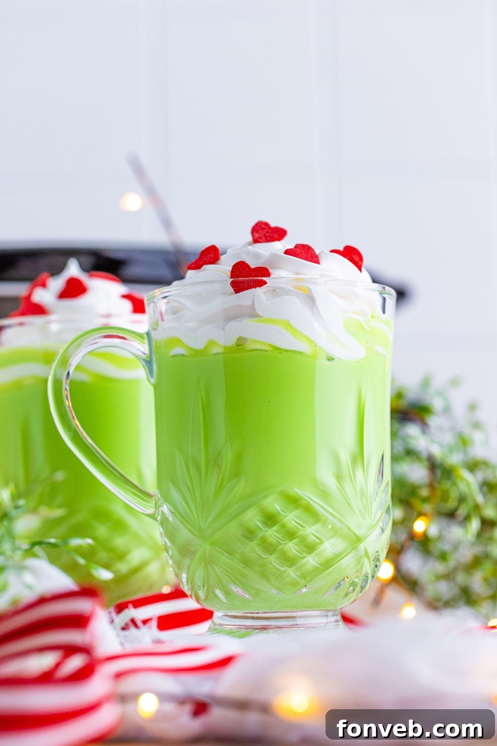 Glasses of green hot chocolate topped with whipped cream and red candy hearts on a table