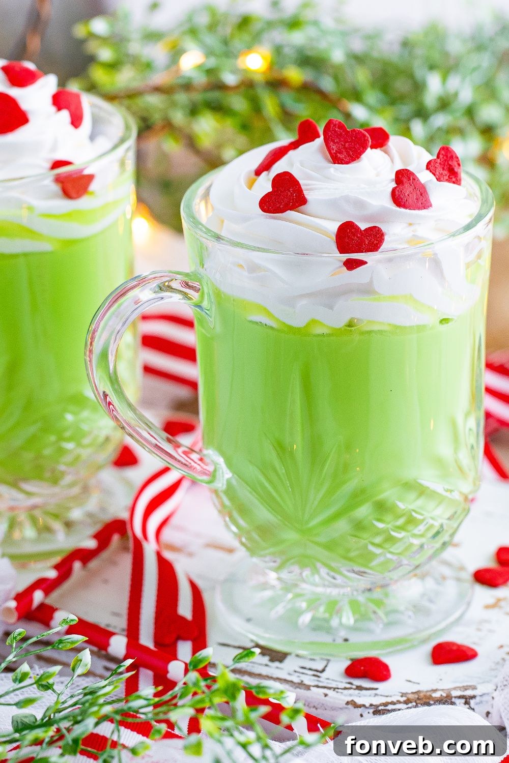 Grinch hot chocolate in glass mugs on a table with a Christmas tree in the background