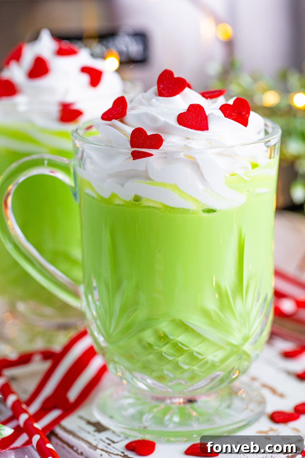 Glasses of green colored hot chocolate with whipped cream and red heart sprinkles in mugs