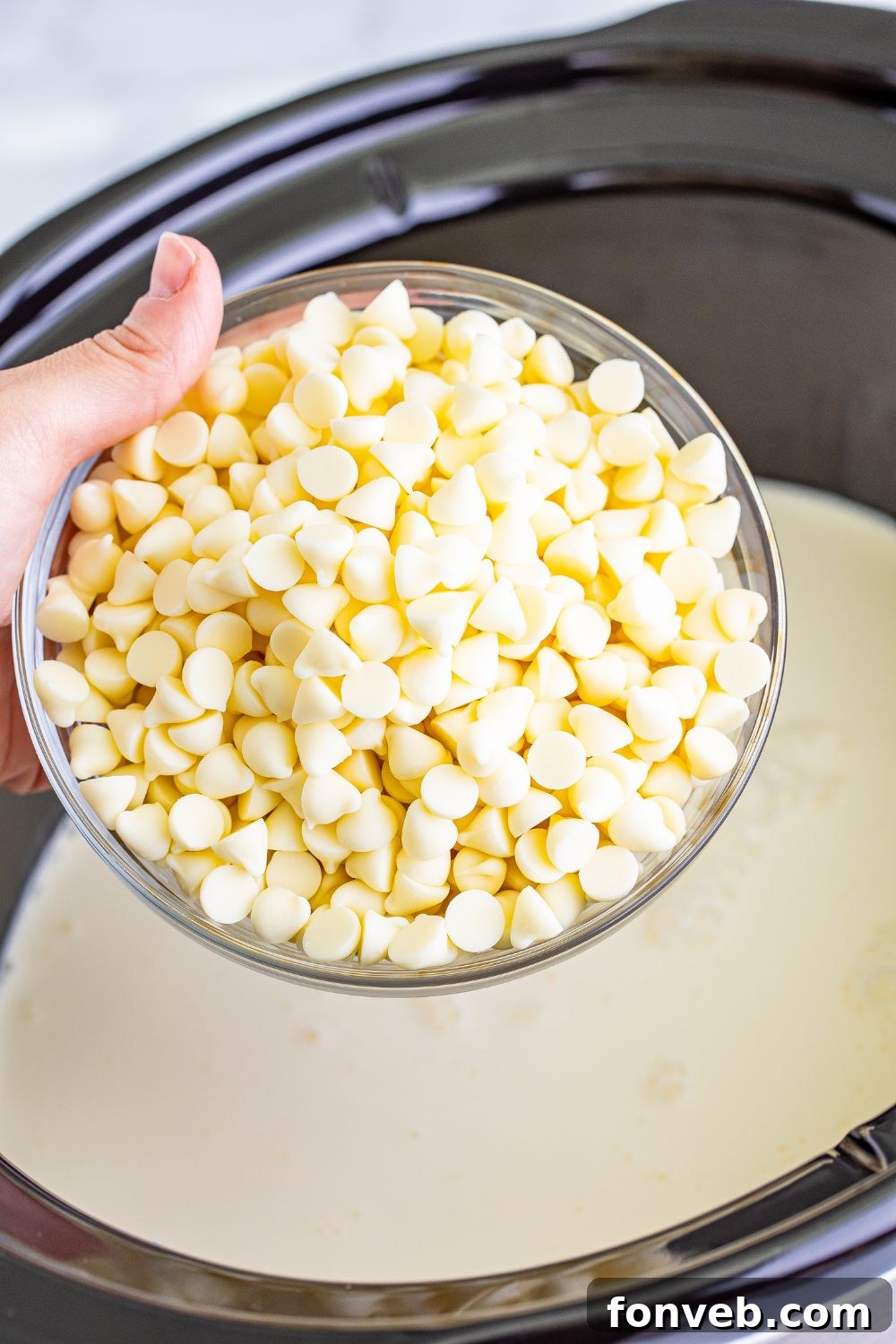 Bowl of white chocolate chips above a slow cooker, ready to be added
