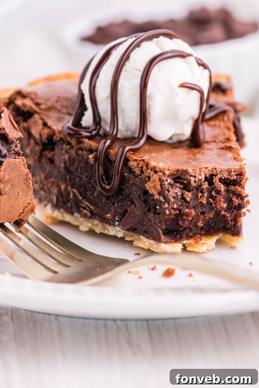 Fudgy Brownie Pie Perfection 12 A tempting slice of brownie pie on a plate, drizzled with hot fudge and topped with a scoop of ice cream.