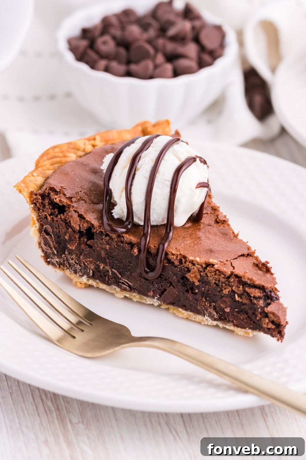 Fudgy Brownie Pie Perfection 13 A slice of brownie pie on a white plate, topped with vanilla ice cream and hot fudge drizzle.