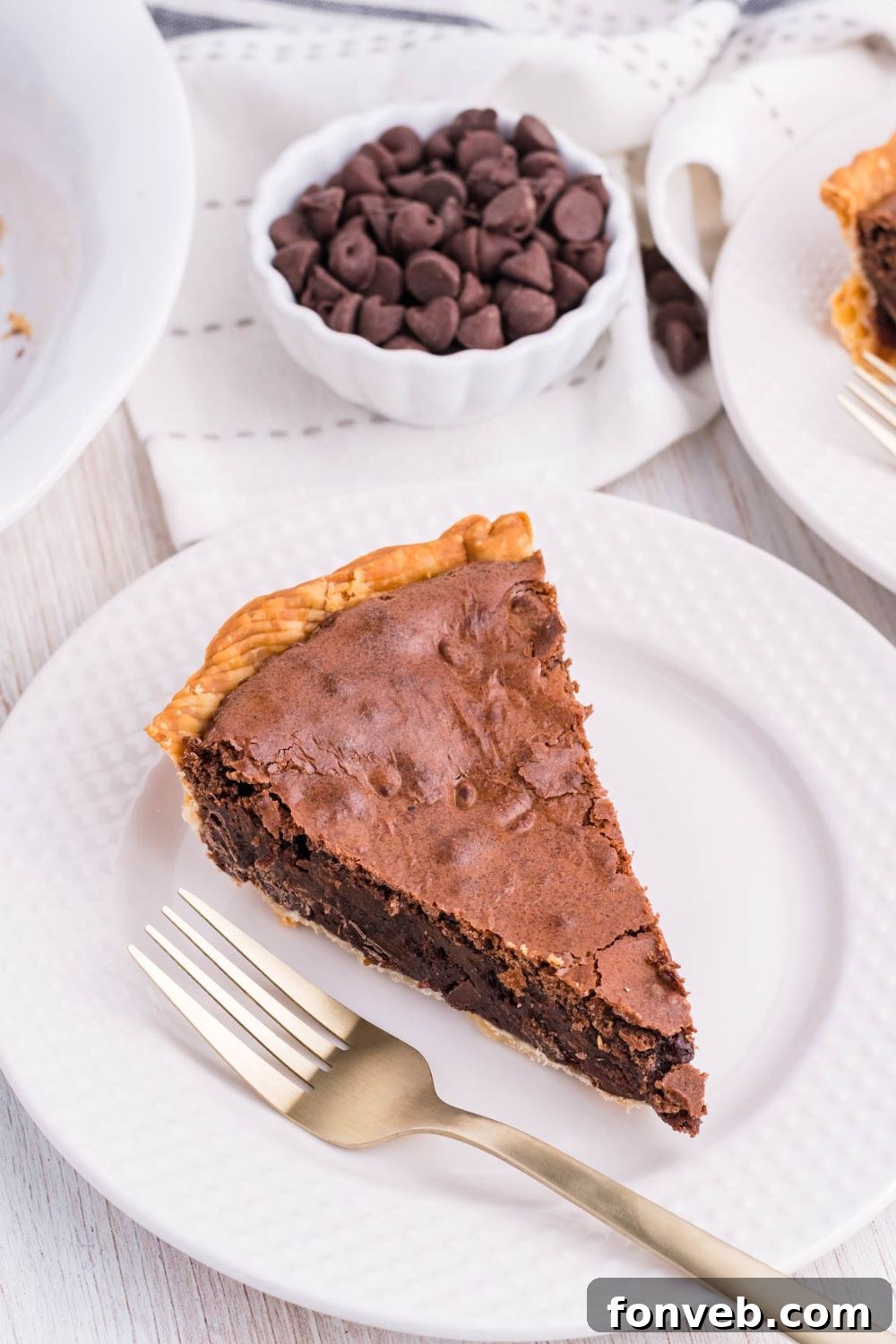 Fudgy Brownie Pie Perfection 17 A slice of rich chocolate pie on a white plate, with a bowl of chocolate chips in the background.