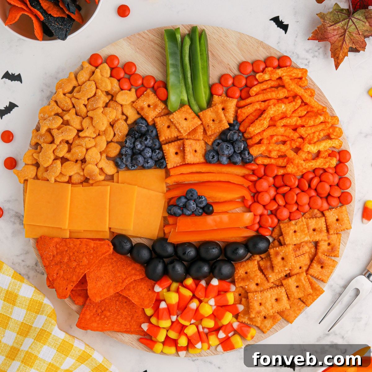 Overhead shot of a vibrant Pumpkin Charcuterie Board shaped like a jack-o-lantern, showcasing orange and dark-colored snacks.