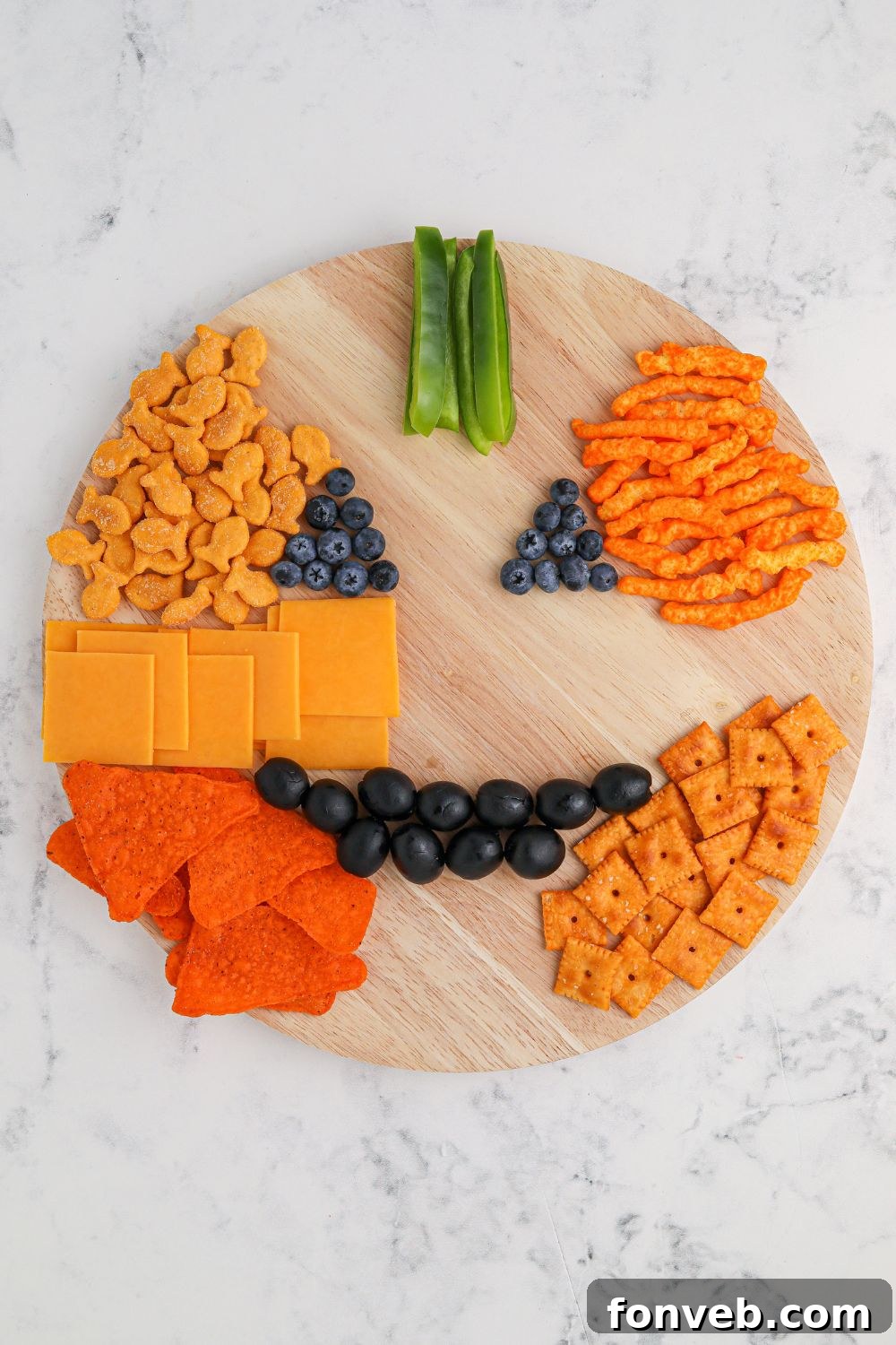 Progress shot of charcuterie assembly on a round board, showing various orange snacks coming together.