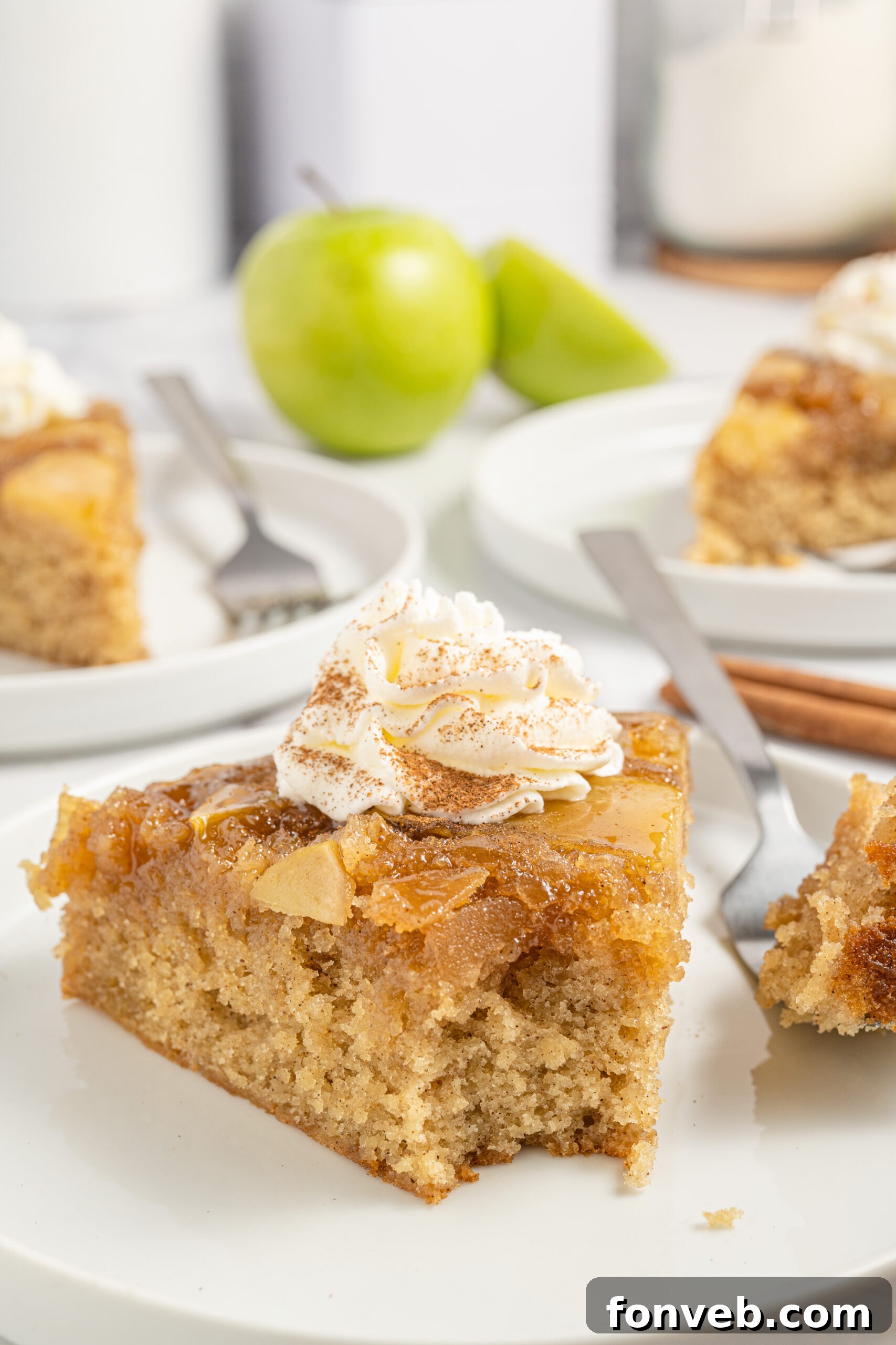 Caramelized Apple Bliss Cake 13 A slice of apple spice cake on a plate with a bite taken out, topped with a dollop of whipped cream