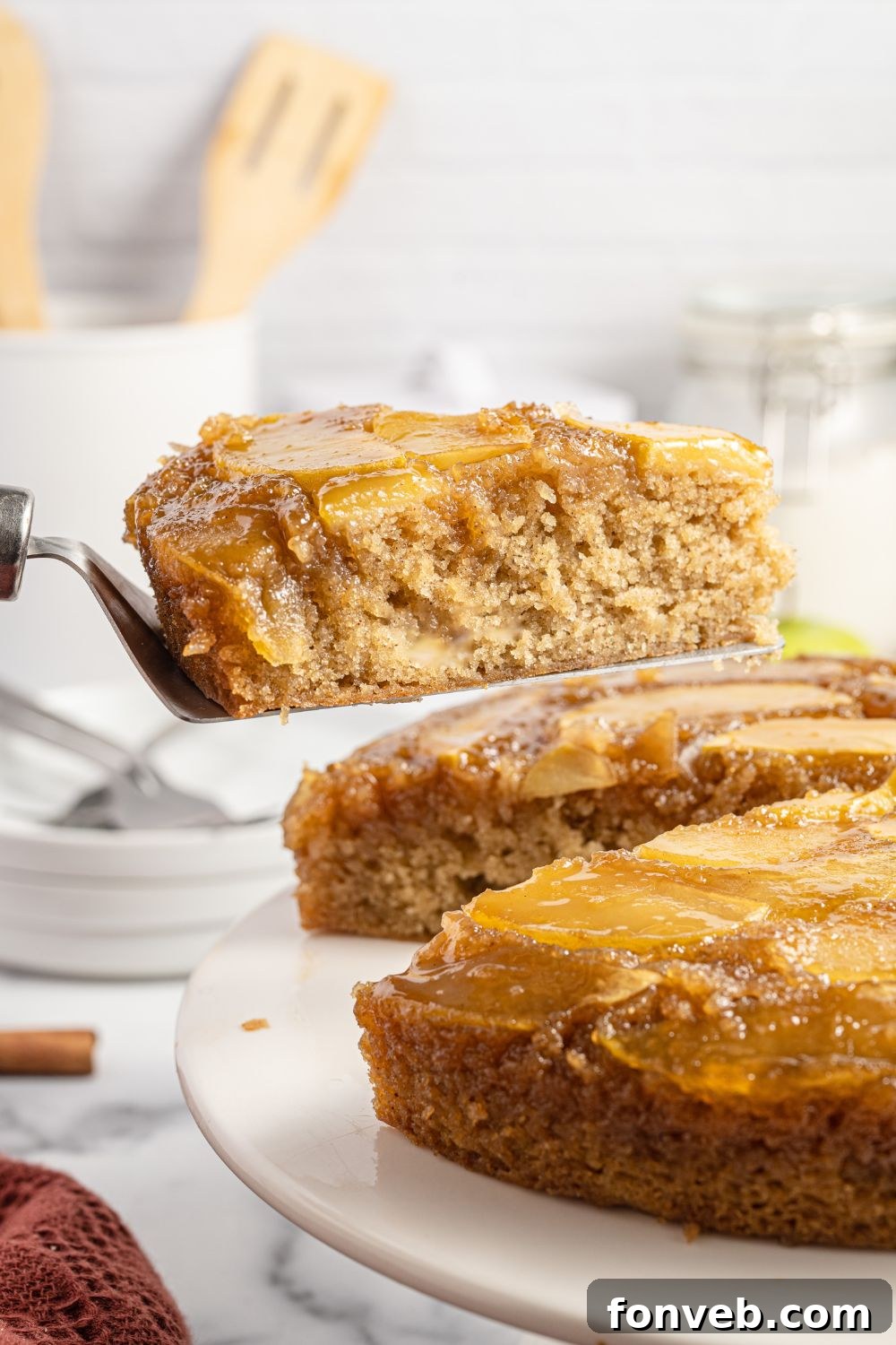 Caramelized Apple Bliss Cake 17 The whole apple upside down cake on a platter, with a single slice being carefully removed with a spatula