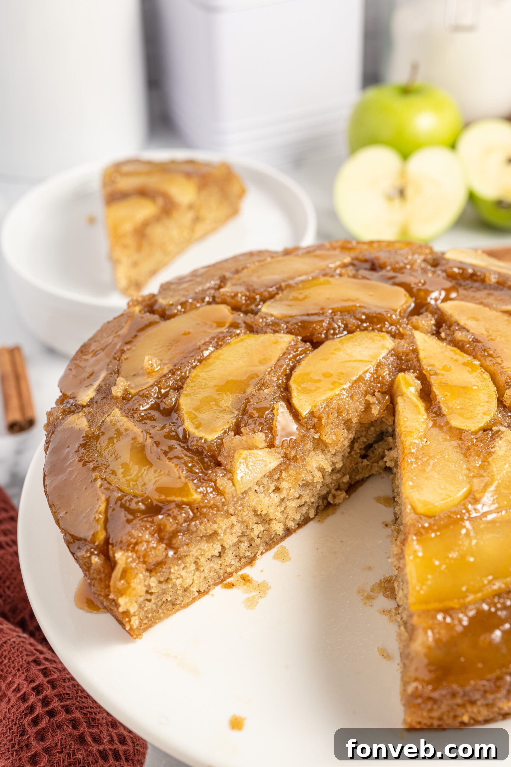 Caramelized Apple Bliss Cake 22 The apple upside down cake on a white serving platter, with a slice removed to display its moist texture and apple topping