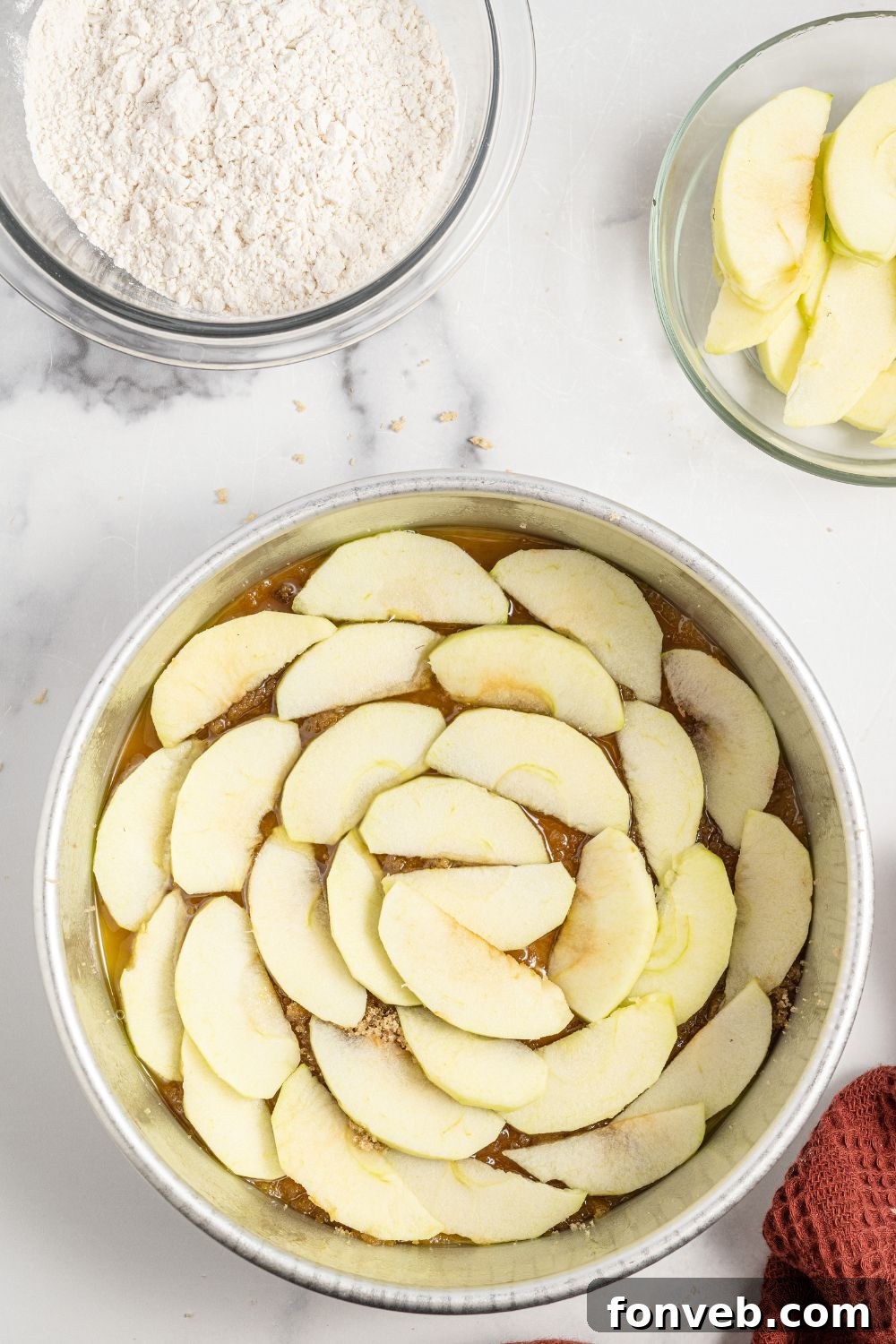 Caramelized Apple Bliss Cake 7 Thinly sliced apples arranged in a circular pattern over the butter and sugar mixture in a cake pan