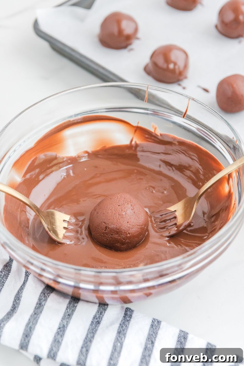 A brownie ball being dipped into melted chocolate using a fork