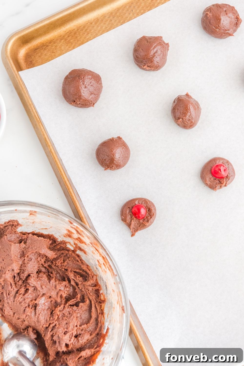 Brownie bites on a cookie sheet with a maraschino cherry placed in the center of each ball