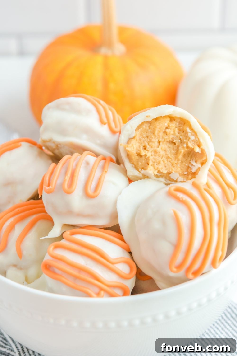Two white chocolate pumpkin truffles in a bowl, one cut in half revealing the creamy pumpkin spice center.