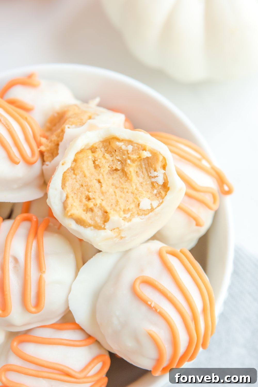 A pumpkin truffle with a bite taken out, resting in a bowl, showcasing its delicious interior.